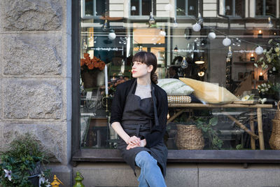 Young female owner sitting with legs crossed on store window sill