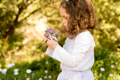 Side view of girl holding flower against trees
