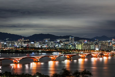 Illuminated bridge over river against sky at night