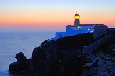 Lighthouse by sea against sky during sunset