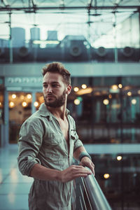 Side view of thoughtful handsome mid adult man looking away while standing by railing in building