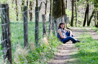 Woman sitting by chainlink fence in forest