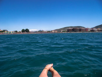 Low section of man by sea against clear blue sky