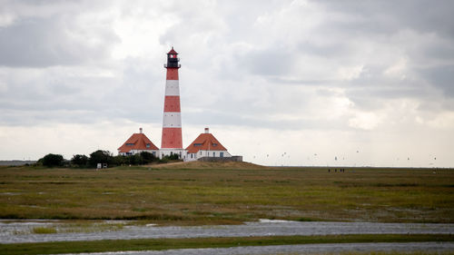 Lighthouse on field by building against sky