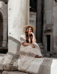 Young woman in beautiful dress sitting on wall of diocletian's palace in split, croatia.