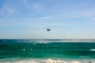 Rescue helicopter flying over sea against sky