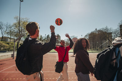 Men playing with ball while walking with friends in sports court on sunny day