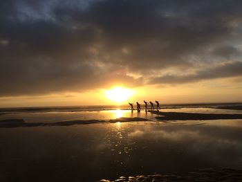 Silhouette men on beach against sky during sunset