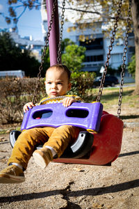 Cute baby boy having fun on outdoor playground. toddler activities. serious baby swinging on swing.