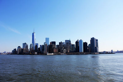 Manhattan city at waterfront against blue sky