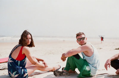 Young couple sitting on beach against clear sky