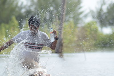 Young man splashing water while running during sunny day