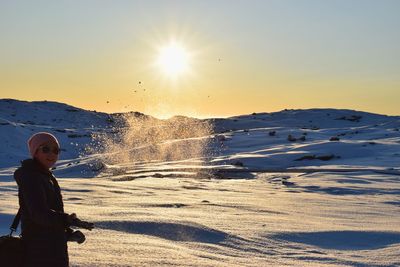 Woman standing on shore against clear sky during sunset