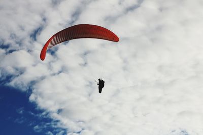 Low angle view of person paragliding against cloudy sky