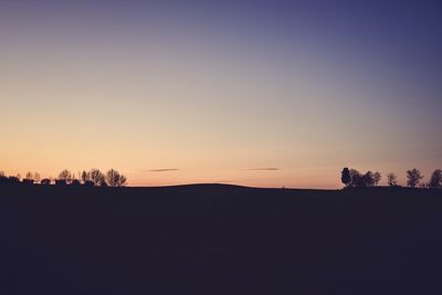 Silhouette trees on field against clear sky