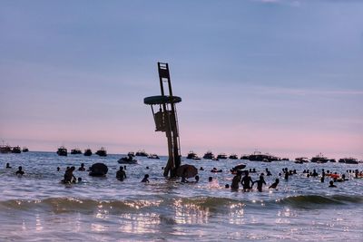 People enjoying at beach against sky during sunset