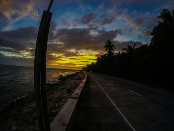 Road by trees against sky during sunset