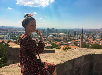 Young woman standing by buildings in city against sky