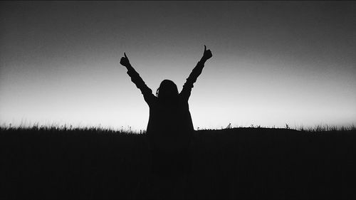 Silhouette woman with arms raised on field against clear sky