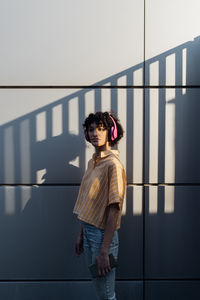 Woman with headphones standing in front of wall with shadow