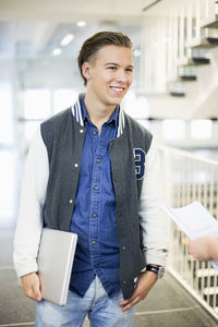 Happy male university student with laptop in college corridor