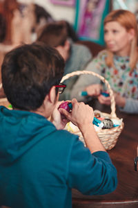 Rear view of young man decorating easter eggs while sitting on table indoors