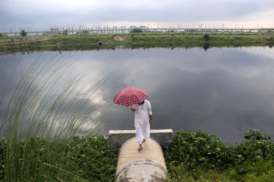 Woman standing on field by water against sky