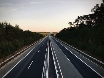 Road by trees against sky during sunset