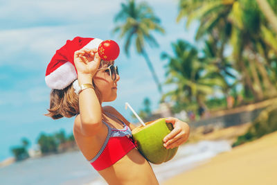 Girl holding christmas ornament and coconut at beach