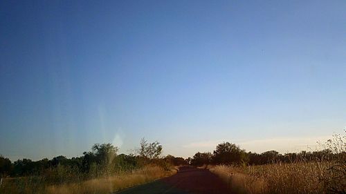 Road amidst field against clear blue sky