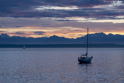 Moored sailboat off shore at sunset under beautiful olympic mountains.