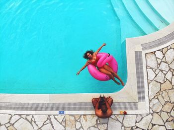 High angle view of woman swimming in pool while man sitting on poolside