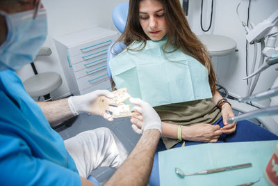 Midsection of dentist holding dental equipment by patient in clinic