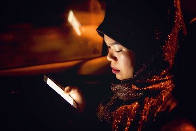 Young woman wearing hijab while using smart phone in car at night