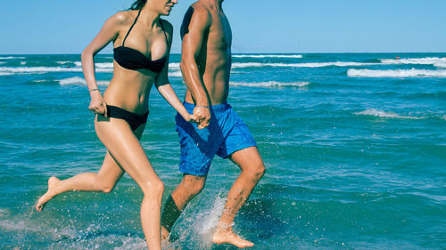 Young woman in bikini on beach against blue sky