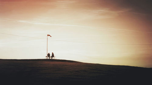 Silhouette couple sitting against sky during sunset