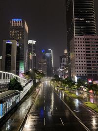 Illuminated street amidst buildings against sky at night