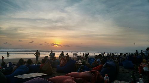People relaxing at beach against sky during sunset
