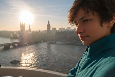 Portrait of man looking at city by river against sky