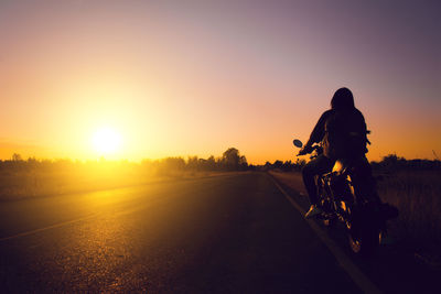 Rear view of woman riding bicycle on road during sunset