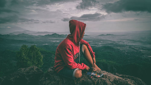 Woman sitting on rock looking at mountain against sky