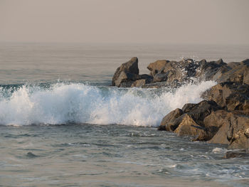 Waves splashing on rocks at shore against sky