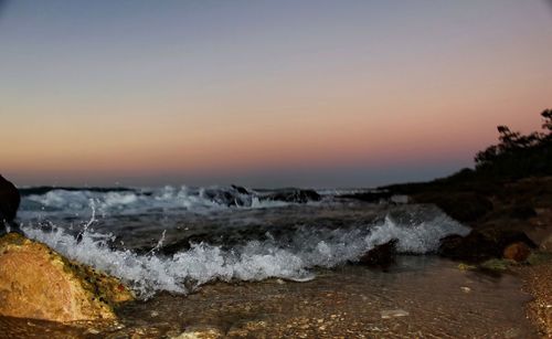 Waves splashing on sea against sky during sunset