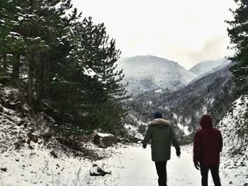 Rear view of two people walking on snow covered mountain during winter