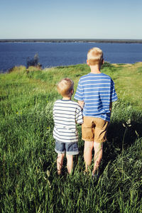 Rear view of brothers standing on grassy field during sunny day