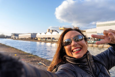 Middle aged woman wearing winter clothes taking selfie by a river - concept of people in recreation