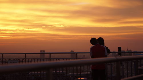 Rear view of silhouette people on railing against orange sunset sky