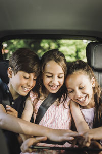 Happy siblings sharing tablet pc while while traveling in car