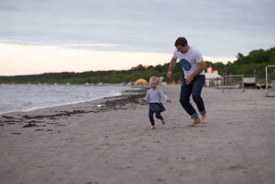 Father and daughter playing at beach against sky