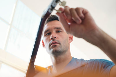 Low angle view of man holding guitar sitting at home